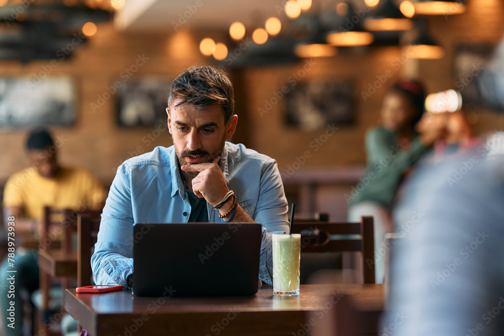 Pensive man using laptop while sitting in cafe. Pensive man using laptop while sitting in cafe.