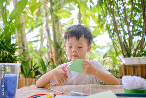 Cute Asian kindergarten boy cutting a piece of paper, Introduce scissor skills for toddlers, Little kid enjoying doing arts and crafts at home garden backyard on nature, Children's Art Project