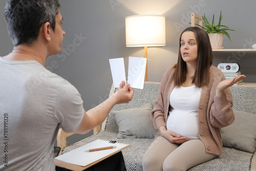 Confused puzzled regnant woman visiting psychologist doctor male psychotherapist showing picture to woman client at session in an office female with uncertain face during consultation