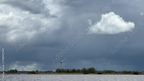 Single windmill on the edge of a lake rotating in storm wind against ominous, dark stom sky, regenerating renewable, sustainable energy and electricity photo