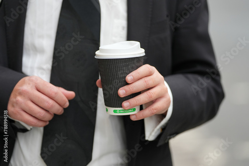 man dressed in a black suit and white shirt holding a recyclable glass. man holding a cup of coffee.