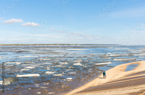 A man and a woman walking along the riverbank in spring, during an ice drift