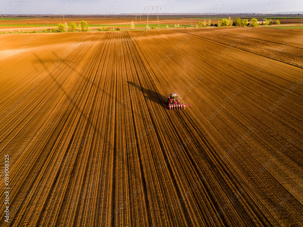 Aerial shot of a farmer seeding, sowing crops at field. Sowing is the process of planting seeds in the ground as part of the early spring time agricultural activities. - obrazy, fototapety, plakaty 