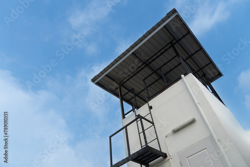 Tall building with stairs for climbing up. The top is covered with a metal cheese roof. For storing water tanks and observation locations. Under blue sky and white clouds.