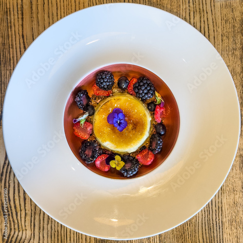 delicious creme brulee beautifully decorated and surrounded with a fruit mix, served on a white plate