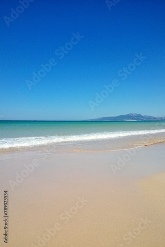 Atlantic ocean and beach with golden sand and blue sky in Tarifa, Spain. Playa de Bolonia on Atlantic coast of Tarifa, Province of Cadiz, Andalucia, southern Spain. Waves on Levante wind on summer day photo