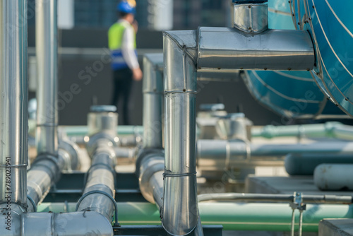 A professional engineer communicates via walkie-talkie on a building's rooftop, surrounded by piping and ductwork. © ultramansk