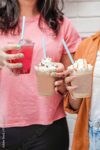Young females holding ice cold drinks frappe coffee and slush in hand.