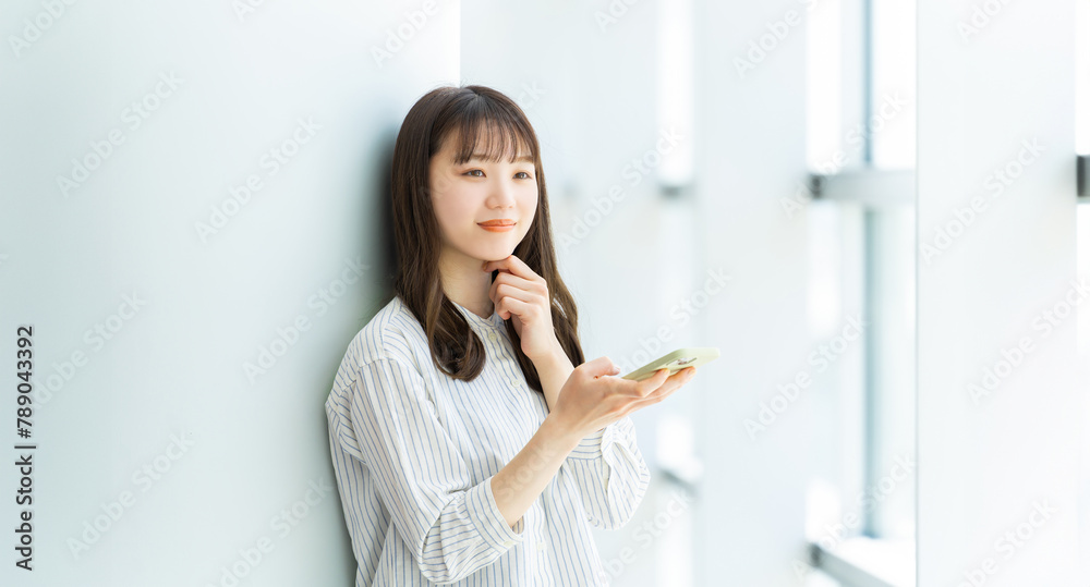 Obraz premium 微笑みながらスマートフォンを使う若い女性