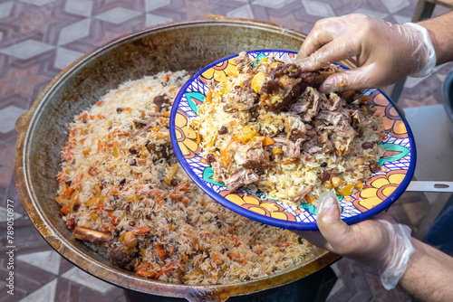 A hand puts meat on a plate of pilaf