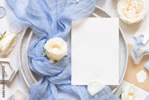 Card near blue tulle fabric knot and cream roses on plates top view copy space, wedding mockup