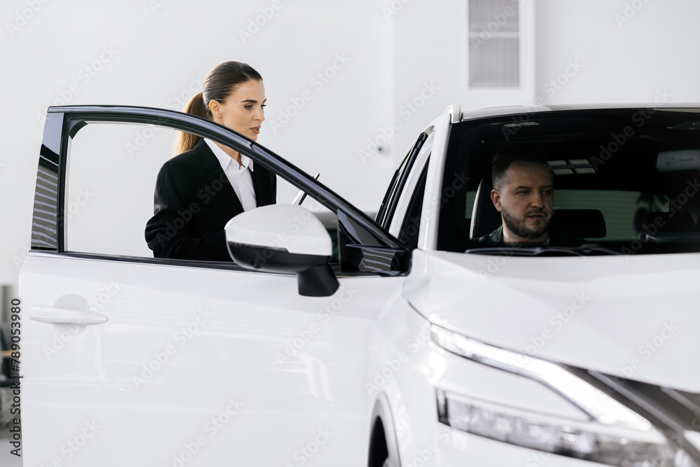 A happy, middle-aged man sits in a modern car and talks to a competent car dealership manager. Choosing a new car. Expensive shopping concept.