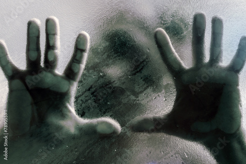 Mans figure with hands pressed against frosted glass. Shadow of a man behind the matte glass blurry hand and body soft focus.