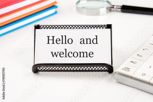 Hello and welcome text on a white business card on a table with office supplies