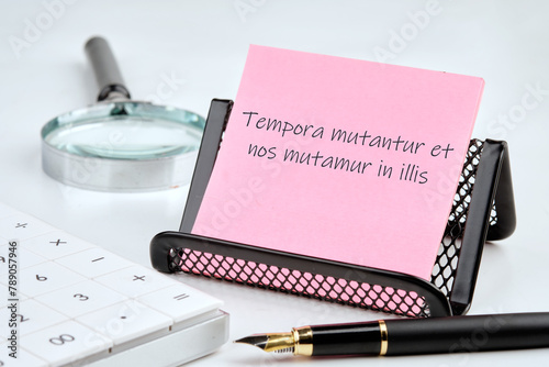 Tempora mutantur et nos mutamur in illis Translated from Latin, it means Times are changing, and we are changing with them. on a pink sticker with office supplies on a white background photo