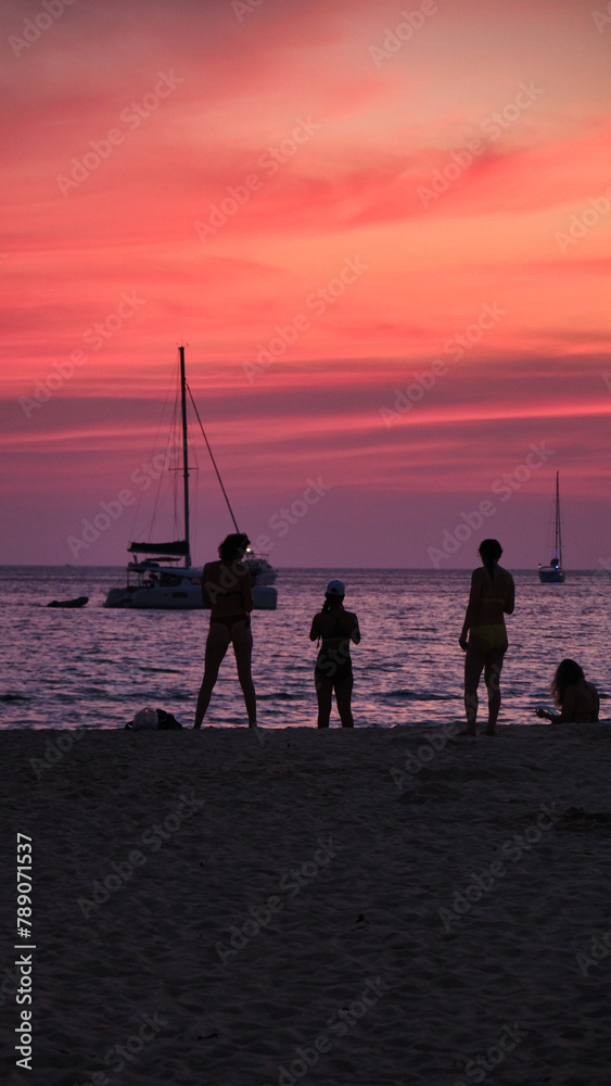 A group of people are standing on the beach at sunset