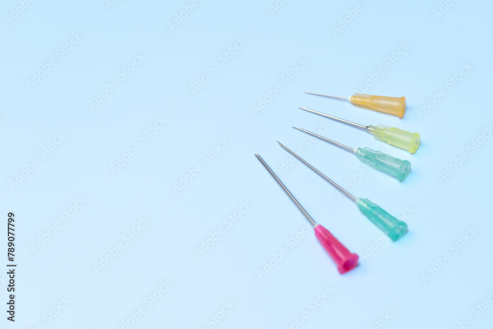 A row of five different colored plastic needles are on a blue background. The needles are of different sizes and colors, with one being green and the others being red, yellow, and blue A row of five different colored plastic needles are on a blue background. The needles are of different sizes and colors, with one being green and the others being red, yellow, and blue