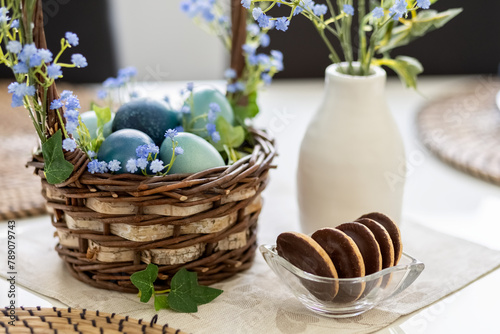 Turquoise and blue Easter eggs in a brown basket on the table. Blue gypsophila flowers in a vase and Easter basket. Card. Photo