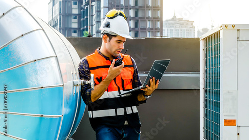 Male technical foreman inspects maintenance working in laptop with to look at plumbing and electrical systems on the roof of a building, maintenance in sewer pipes area at construction site.