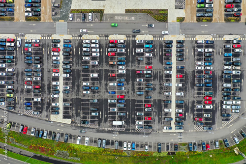 Aerial top view of a busy carpark showing all different kinds of cars parked up and driving on the road looking for a space.