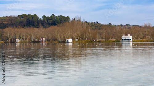 Las aguas tranquilas del Lago de Banyoles reflejan las pesqueras y los árboles sin hojas en una serena tarde de invierno en Pla de l'Estany, Cataluña.