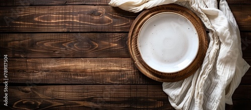 Wooden table background with an empty plate and towel, seen from above, providing space for text.