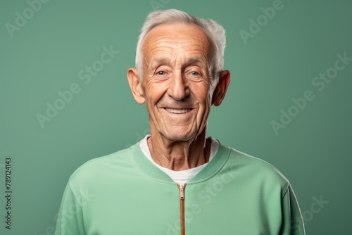 Portrait of a grinning man in his 80s sporting a breathable mesh jersey over solid color backdrop