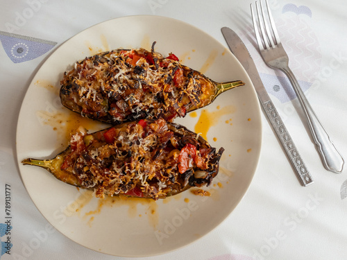 Stuffed eggplant with vegetables , chorizo and cheese topping served on a plate with cutlery.