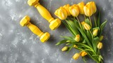 Yellow dumbbells accompanied by a bouquet of tulips stand out against a stylish gray concrete backdrop This vibrant image conveys a message of health and fitness making it a versatile choic