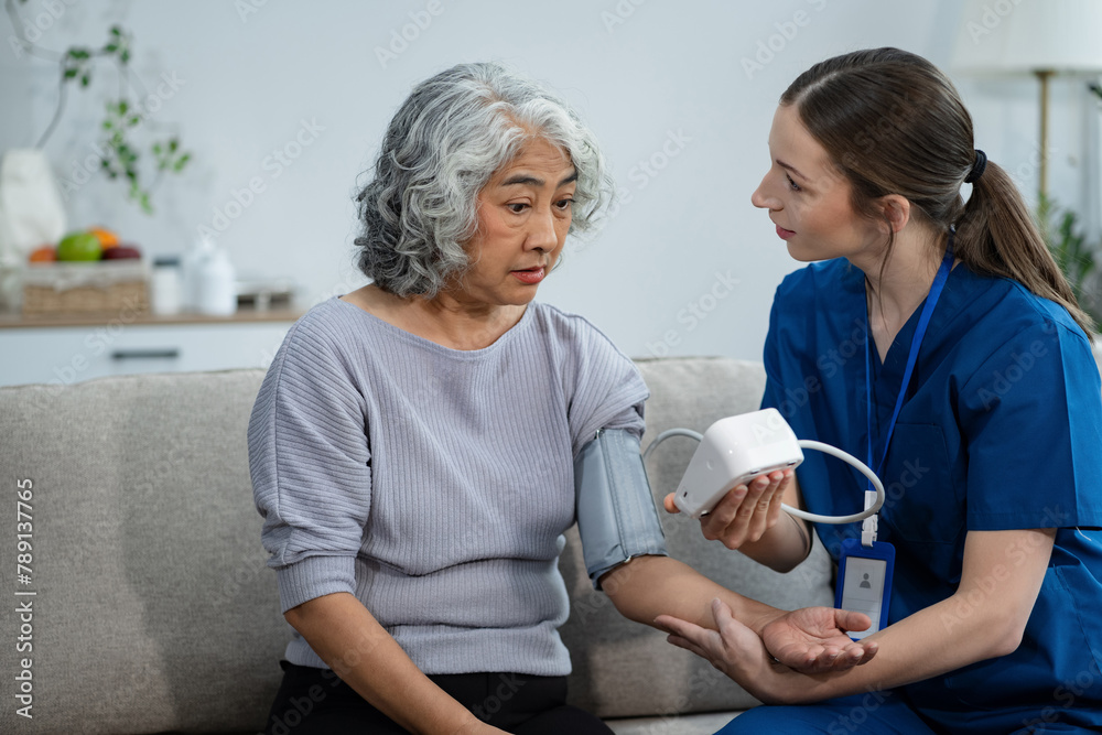 Obraz premium Female doctor checking old woman blood pressure at clinic and filling patient history in the morning.