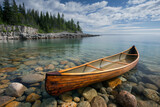 A handmade wooden canoe rests on the pebbled shore of a tranquil lake, with clear waters reflecting a serene, cloud-streaked sky and forested coastline.