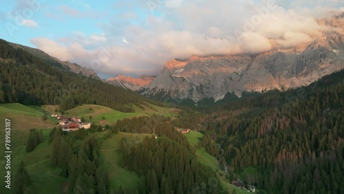 An evening aerial footage of secluded houses of the village of La Val with majestic Sas dles Nü (Cima Nove) mountain covered in beautiful clouds in the background. South Tyrol, Italy. LuPa Creative