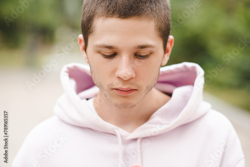 Handsome blond teenage boy 18-20 year old wearing hoodie looking down close up. photo