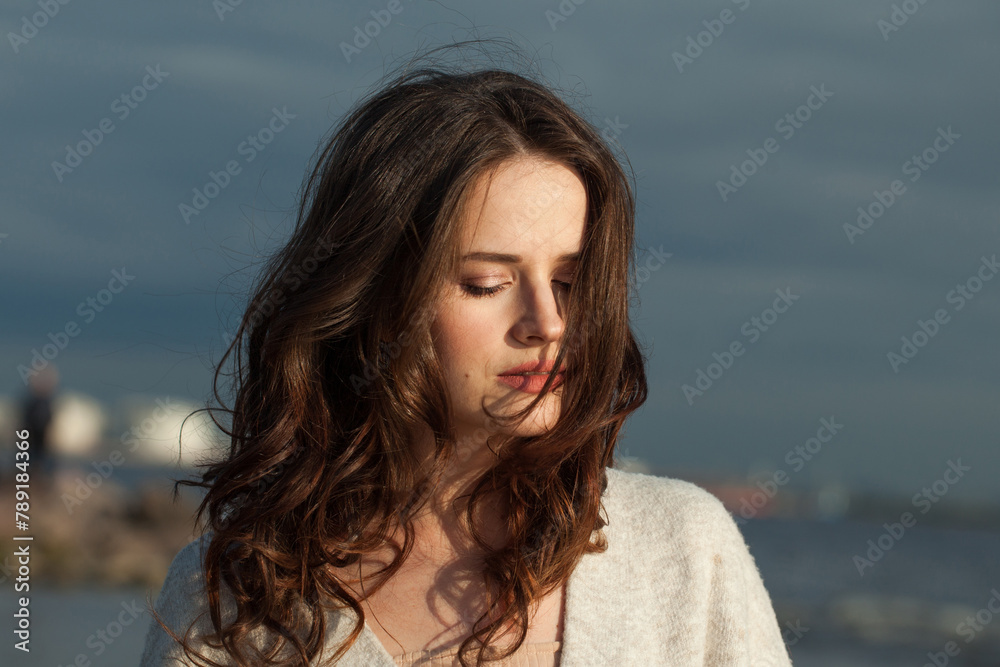 Pretty young woman model with brown hair and natural make-up walking along the shore of the resort on a spring morning. Happiness, balance, tranquility, emotion and mood concept. Eyes closed Pretty young woman model with brown hair and natural make-up walking along the shore of the resort on a spring morning. Happiness, balance, tranquility, emotion and mood concept. Eyes closed