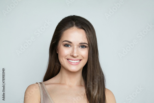 Beautiful young female model with healthy hair, makeup and shiny clear skin posing against gray studio wall background. Facial treatment, cosmetology, hair care and beauty woman concept