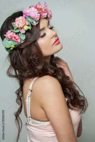 Posing fashion brunette model with make-up, fresh clear skin, shiny long wavy hairstyle and pink spring flower. Skin care, haircare, cosmetology and beauty concept