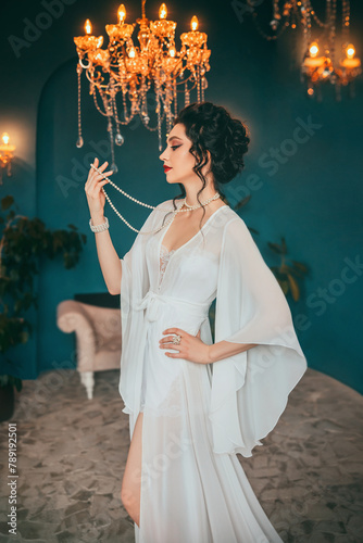 Fantasy woman dark curly elegant hair bun hairstyle. Sexy beauty face girl in luxury room crystal chandelier shines. Long vintage white dress silk peignoir pearl set beads art style photo real person 
