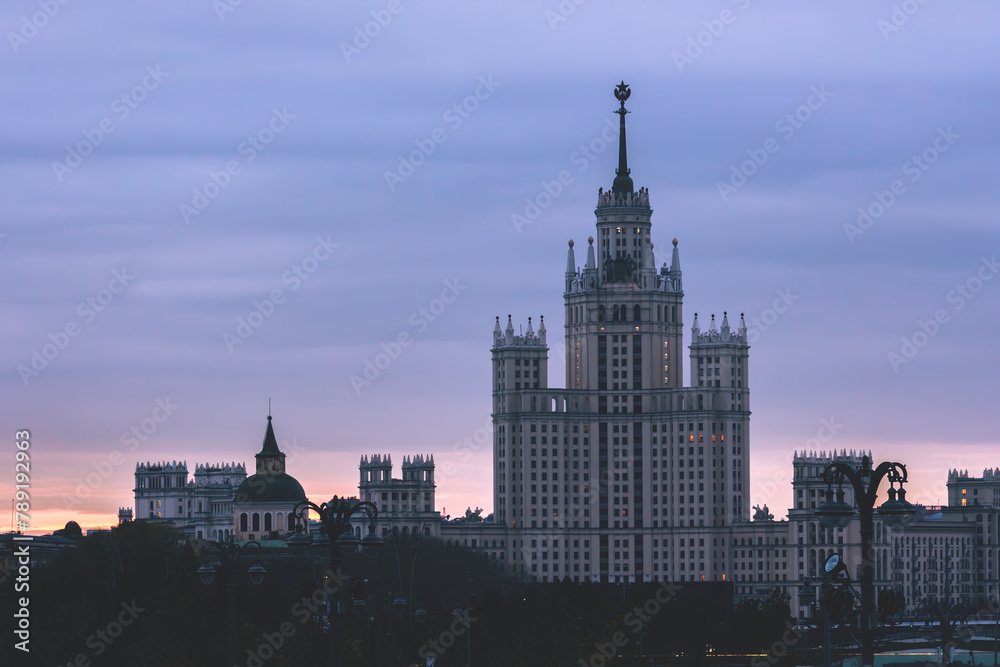 Dawn breaks over Moscow, casting a soft glow on the classic Stalinist architecture of a high-rise building, invoking a serene mood