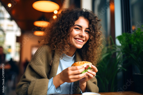 A woman wearing a happy smile is enjoying her hamburger at the table