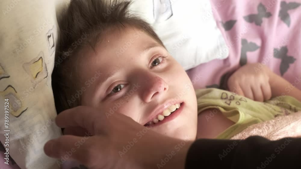 Authentic shot of a teenage girl with Down syndrome, autism. The loving hand of an adult strokes her cheek. Concept: disabled people, child care, healthcare, disability, dreams, life, hope.