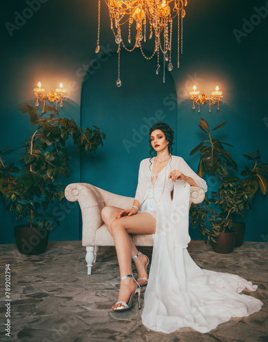 Fantasy woman sitting on throne chair sofa. Sexy beauty face red lips pink make-up dark hair bun girl in luxury room. Long bare legs silver sandals high heel shoes vintage silk white dress art style 