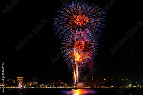 Breathtaking fireworks light up the night sky above a tranquil bay, casting reflections over calm waters. © ultramansk