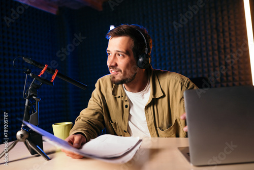 A young man wearing headphones is podcasting in a home studio, holding notes and smiling, representing online content creation and broadcasting.