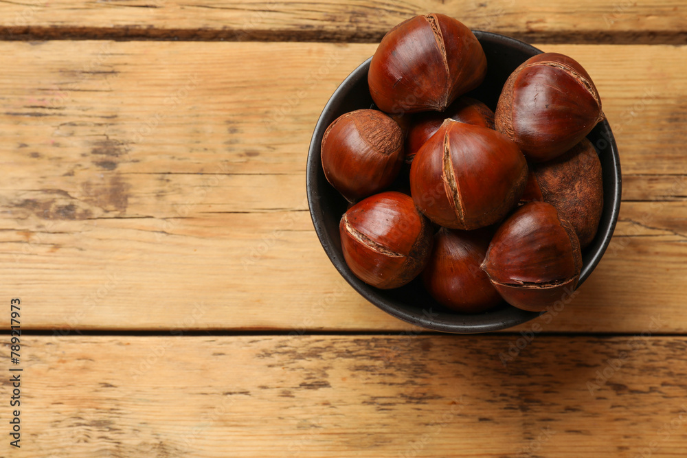 Fresh edible sweet chestnuts in bowl on wooden table, top view. Space for text Fresh edible sweet chestnuts in bowl on wooden table, top view. Space for text
