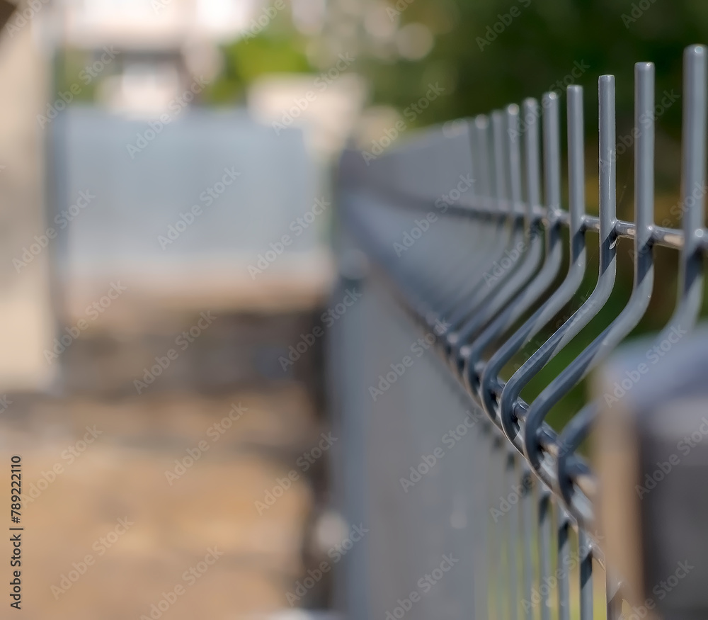 Naklejka premium Ogrodzenie panelowe wykonane z cienkich drutów. Ogrodzenie siatkowe wokół domu w mieście. Dom wśród bogatej zieleni miejskiej.