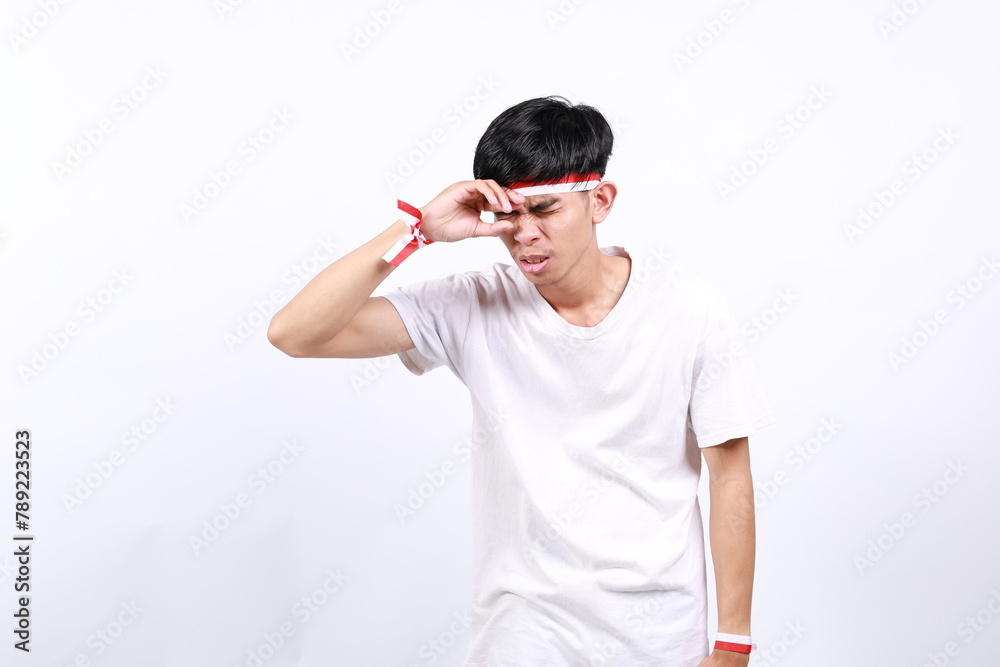 Frustrated asian young boy with red white ribbon for celebrating Indonesia independence day standing while holding head Frustrated asian young boy with red white ribbon for celebrating Indonesia independence day standing while holding head