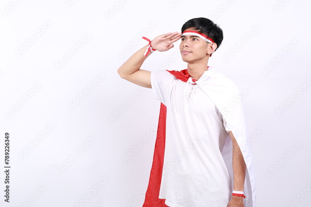 Asian young boy with red white ribbon for celebrating Indonesia independence day standing with salute hand gesture while looking side above Asian young boy with red white ribbon for celebrating Indonesia independence day standing with salute hand gesture while looking side above