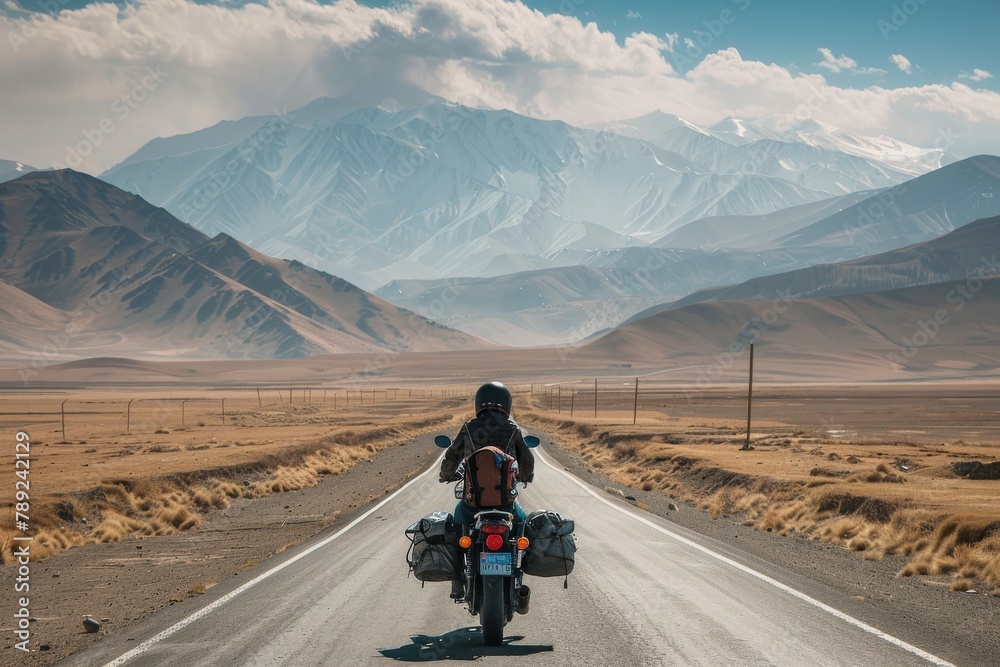 Adventurous journey of a motorcyclist riding on an open road with a breathtaking view of snowy mountains under a clear sky