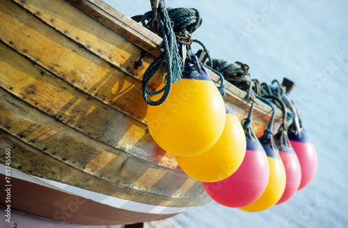 Horizontal image of yellow and red boat buoys hanging from the side of an old wooden boat. location Cromer Norfolk UK