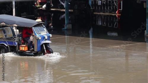 A traditional motorized tricycle - tuk tuk drives through a flooded street, Thailand photo
